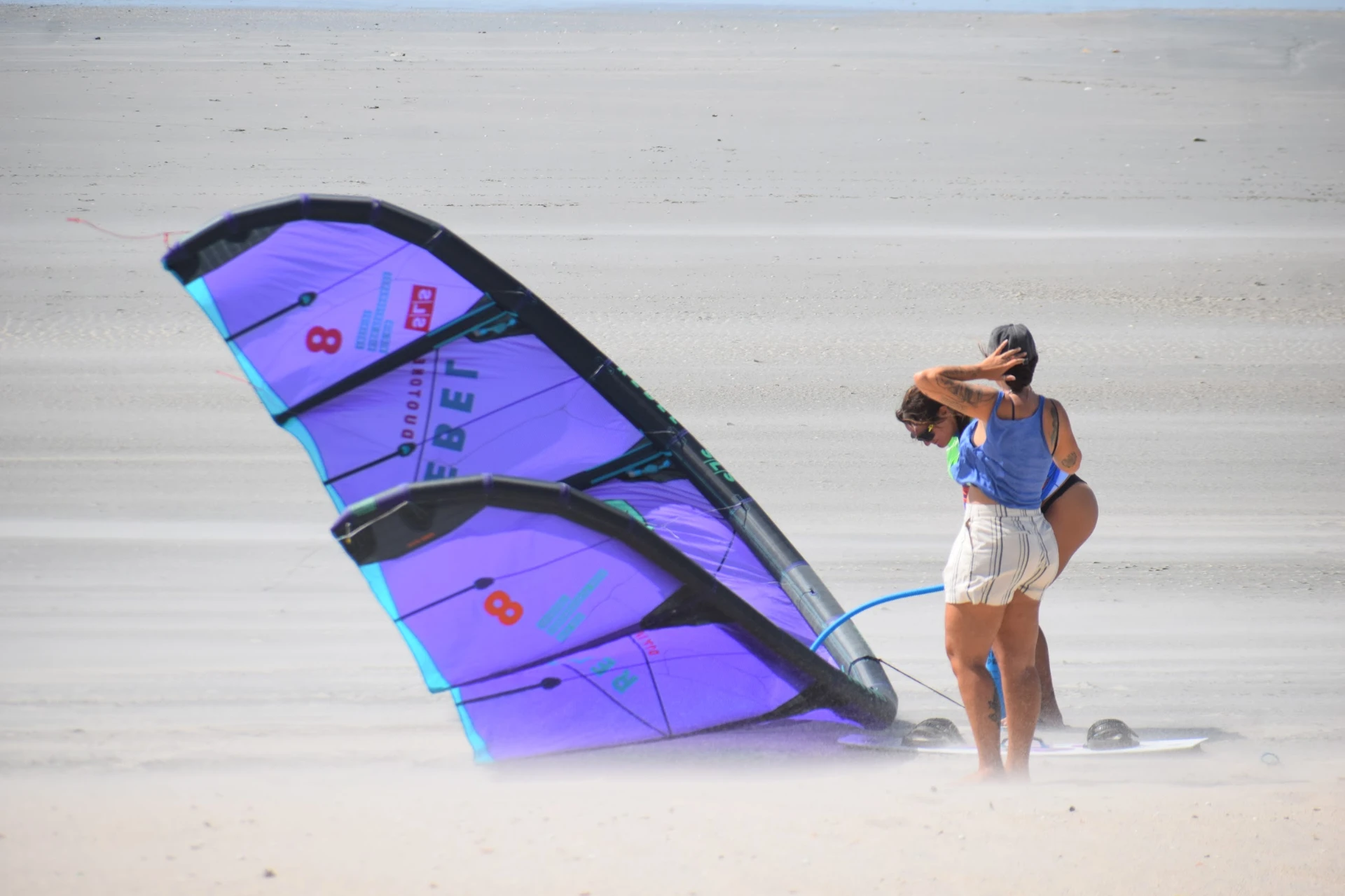 Duas mulheres com pipas de kitesurf roxas na areia da praia